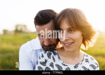 Man embracing PRegnant woman on field against sky Stock Photo