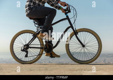 Low section of man riding bicycle on retaining wall against clear blue sky during sunny day Stock Photo