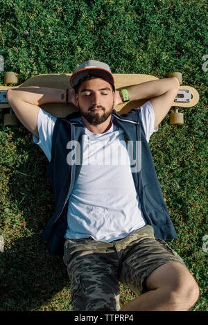 High angle view of handsome man with skateboard lying on grassy field at park Stock Photo
