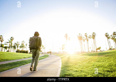 Rear view of man with backpack walking on footpath during sunny day Stock Photo