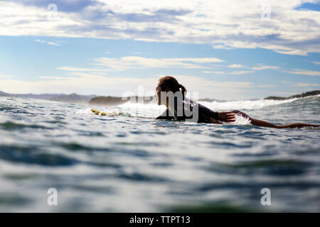 Side view of female surfer lying on surfboard in sea Stock Photo