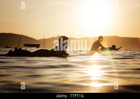 Female surfer lying on surfboard in sea during sunset Stock Photo