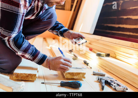 Midsection of carpenter photographing through phone while working in workshop Stock Photo