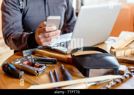 Midsection of carpenter using mobile phone at table in workshop Stock Photo