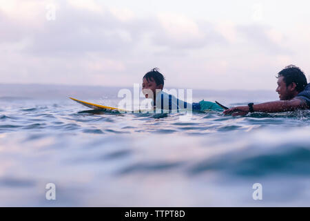 Father and son surfing in sea against sky Stock Photo
