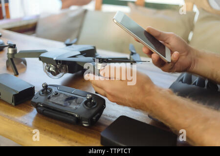 Cropped hands of engineer using mobile phone while examining quadcopter on table at office Stock Photo