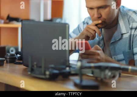 Engineer using mobile phone while sitting at table in office Stock Photo