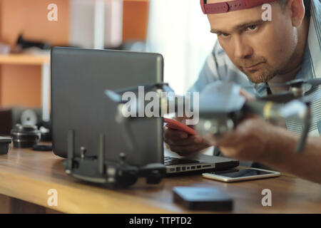 Engineer using mobile phone while examining quadcopter at table in office Stock Photo