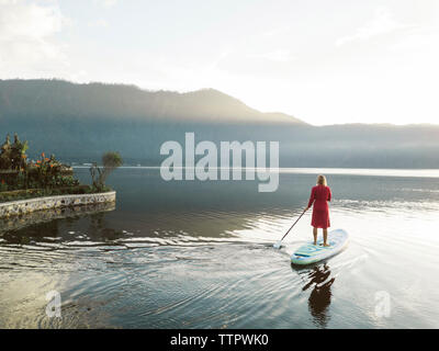 A female paddleboarding on a lake at sunrise Stock Photo