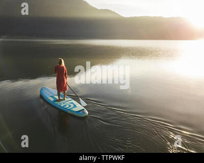 A female paddleboarding on a lake at sunrise Stock Photo