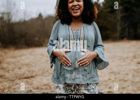 Portrait of happy pregnant woman touching belly while standing in forest Stock Photo