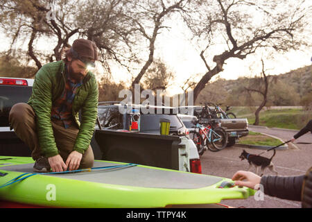 Man tying paddleboard on pick-up truck during vacations Stock Photo