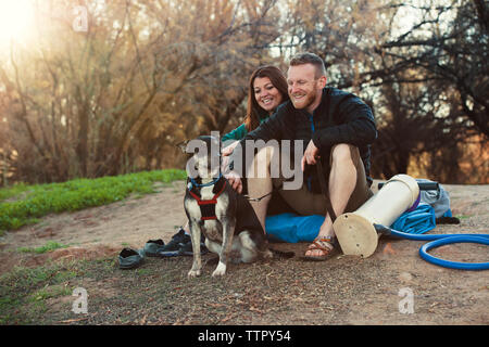 Happy couple looking at dog in forest Stock Photo