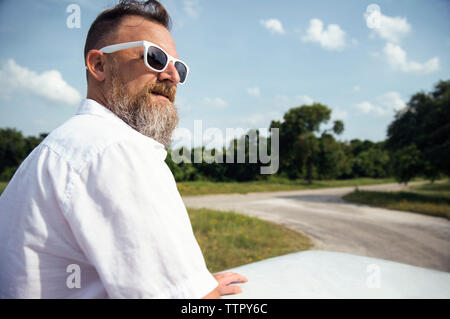 Thoughtful man in sunglasses looking away while standing against sky Stock Photo