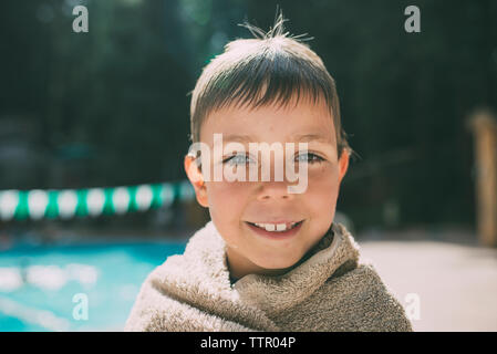 Portrait of happy boy wrapped in a towel standing at poolside Stock Photo