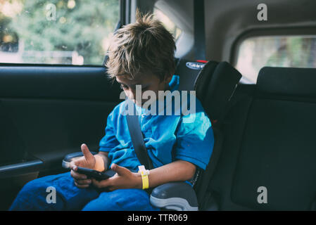 Boy using smart phone while sitting in car Stock Photo