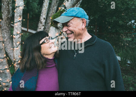 Happy senior couple looking face to face against decorated tree trunk at yard Stock Photo