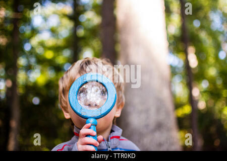 Boy looking through magnifying glass in forest Stock Photo