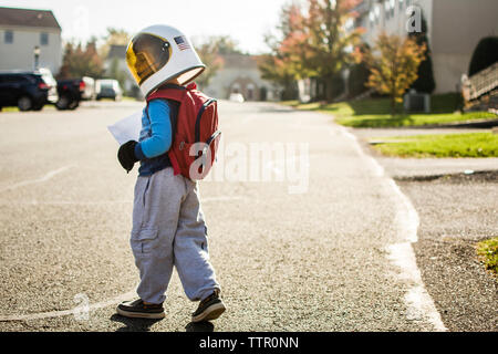 Boy wearing space helmet walking on road in city Stock Photo