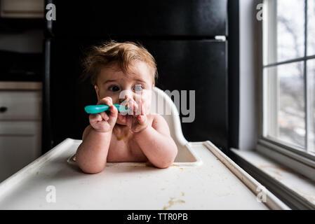 Close up of messy baby in highchair eating with spoon Stock Photo
