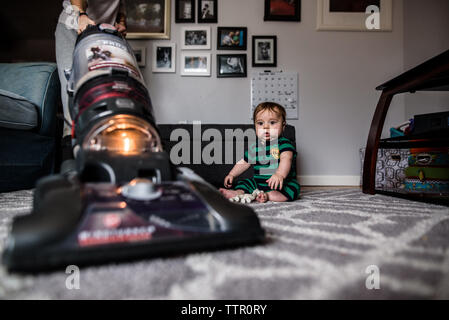 startled baby watches as mother vacuums the rug he is sitting on Stock Photo