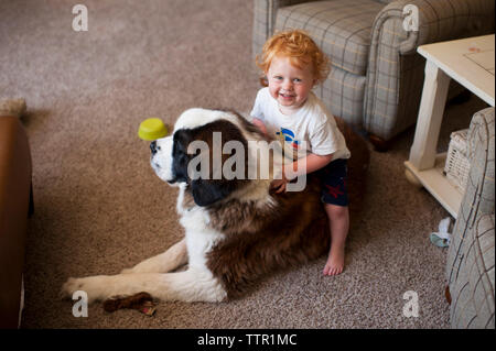 High angle portrait of cute happy baby boy sitting on dog at home Stock Photo