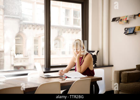 businesswoman reading file at desk by window in creative office Stock Photo