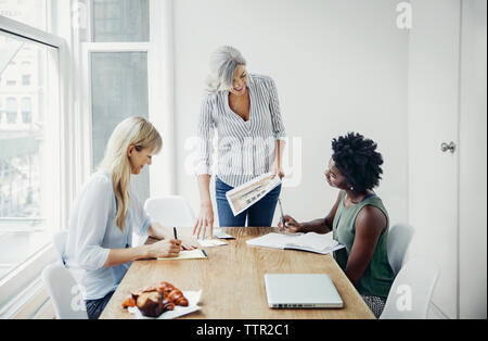 Mature businesswoman discussing over documents with female colleagues in board room Stock Photo