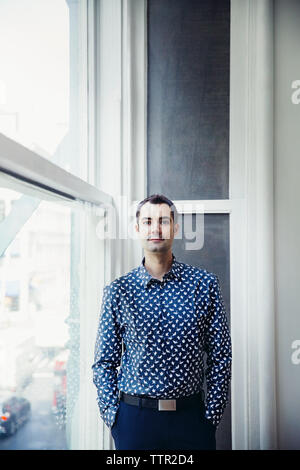 Portrait of confident businessman standing by window in creative office Stock Photo