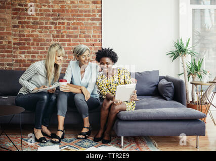 Happy businesswomen using tablet computer while sitting on sofa in creative office Stock Photo