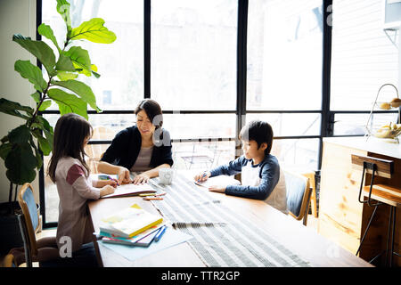 Mother teaching children on table against window at home Stock Photo