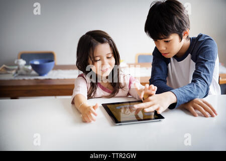 Siblings using digital tablet on table at home Stock Photo