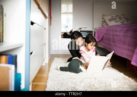 Mother teaching daughter while sitting on carpet in bedroom Stock Photo