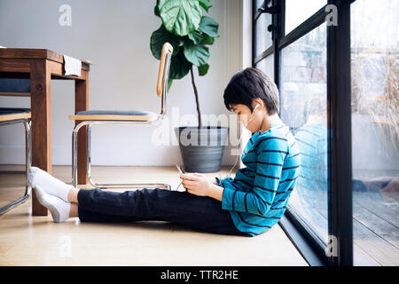 Boy using digital tablet while sitting by window Stock Photo