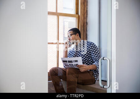 businessman holding document and talking on mobile phone seen through glass Stock Photo