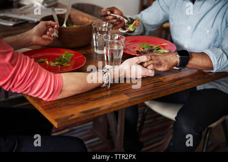 Midsection of gay couple holding hands while eating salad at dining table Stock Photo