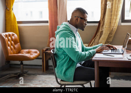 Side view of man using laptop at table Stock Photo
