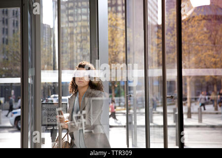 businesswoman opening revolving door while entering modern building Stock Photo
