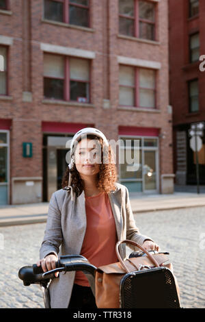 Portrait of confident businesswoman holding bicycle on street Stock Photo