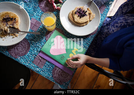 Overhead view of woman eating pancakes by greeting cards on table on birthday