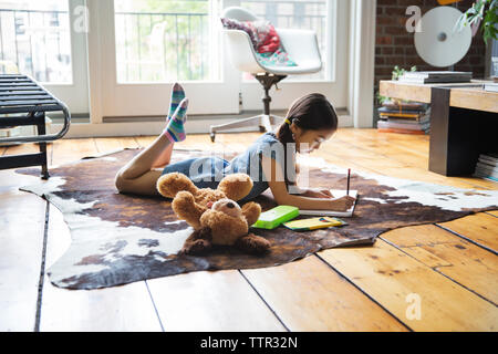 Girl lying on carpet and writing on book at home Stock Photo