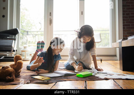 Happy sisters studying on carpet at home Stock Photo