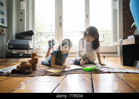 Sisters writing in book on carpet at home Stock Photo
