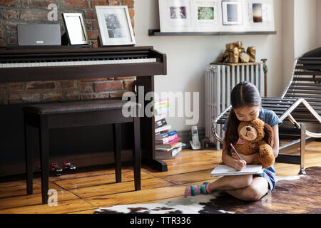 Girl writing in book while sitting on carpet at home Stock Photo