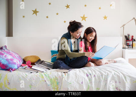 Mother and daughter reading book while sitting on bed at home Stock Photo