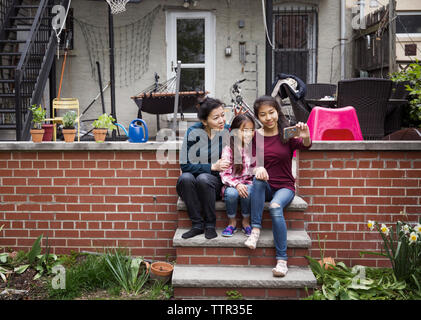 Family taking selfie while sitting on steps outside house Stock Photo