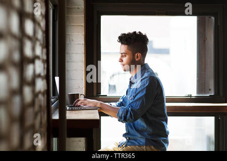 Side view of serious man using laptop while sitting by windows at cafe Stock Photo