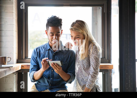 Smiling couple using mobile phone while sitting by window at cafe Stock Photo