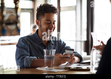 Smiling young man using phone at bar counter in cafe Stock Photo