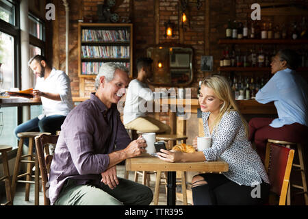 Woman showing phone to man while customers relaxing at cafe Stock Photo